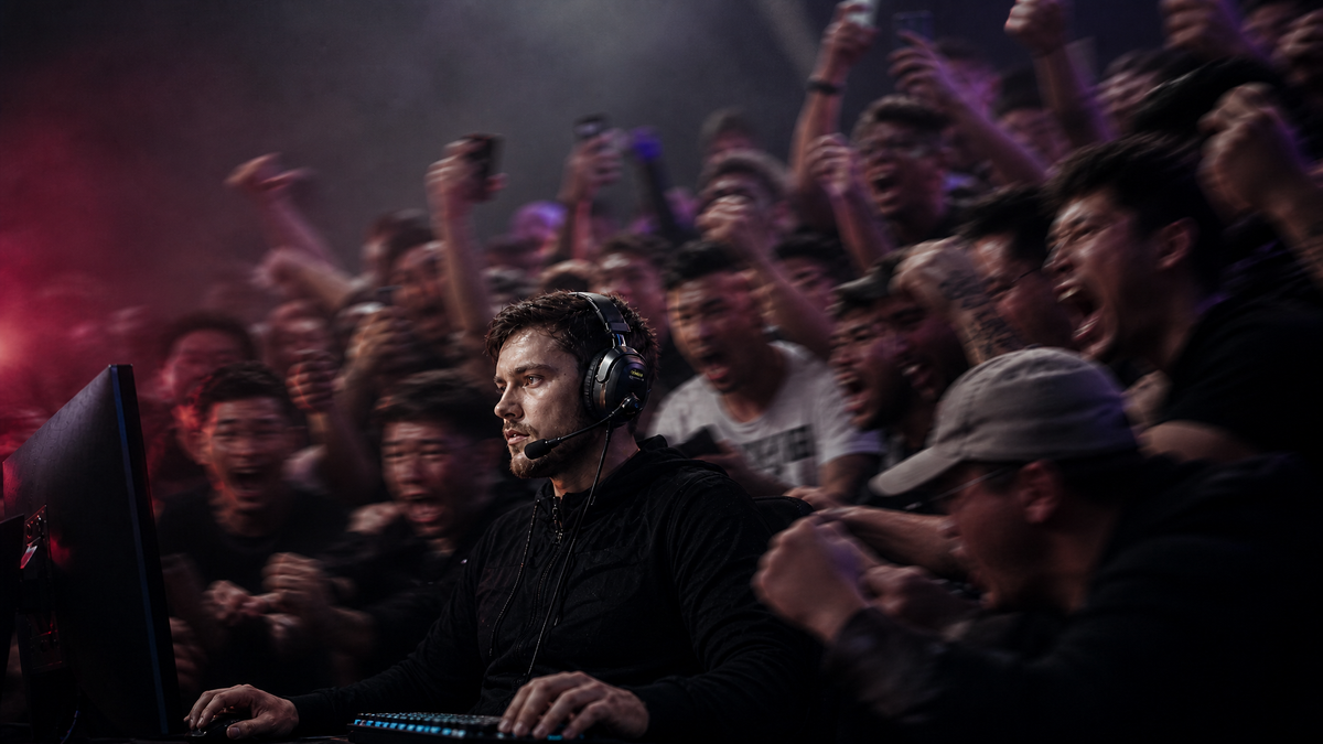 Esports player in a headset stays focused while the crowd behind him erupts